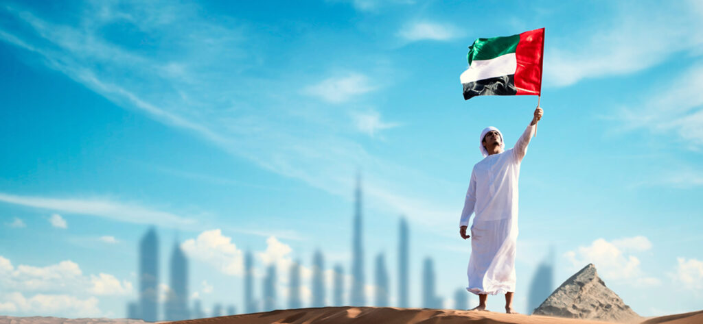 A man holding up the UAE flag with the Dubai skyline in the background.